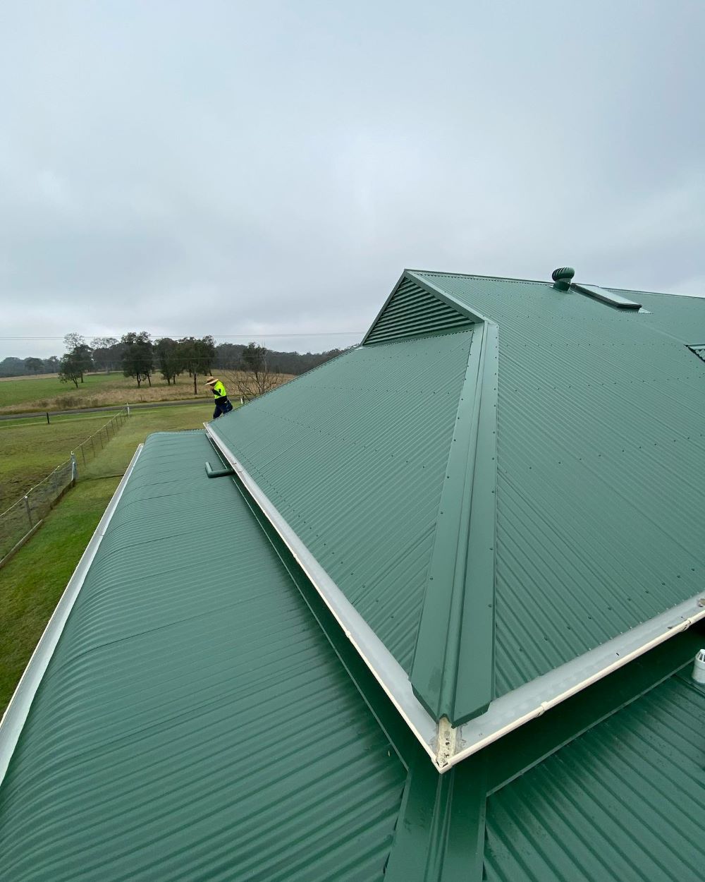A Man is Standing on Top of a Green Roof — Lake Valley Roofing in Cardiff, NSW
