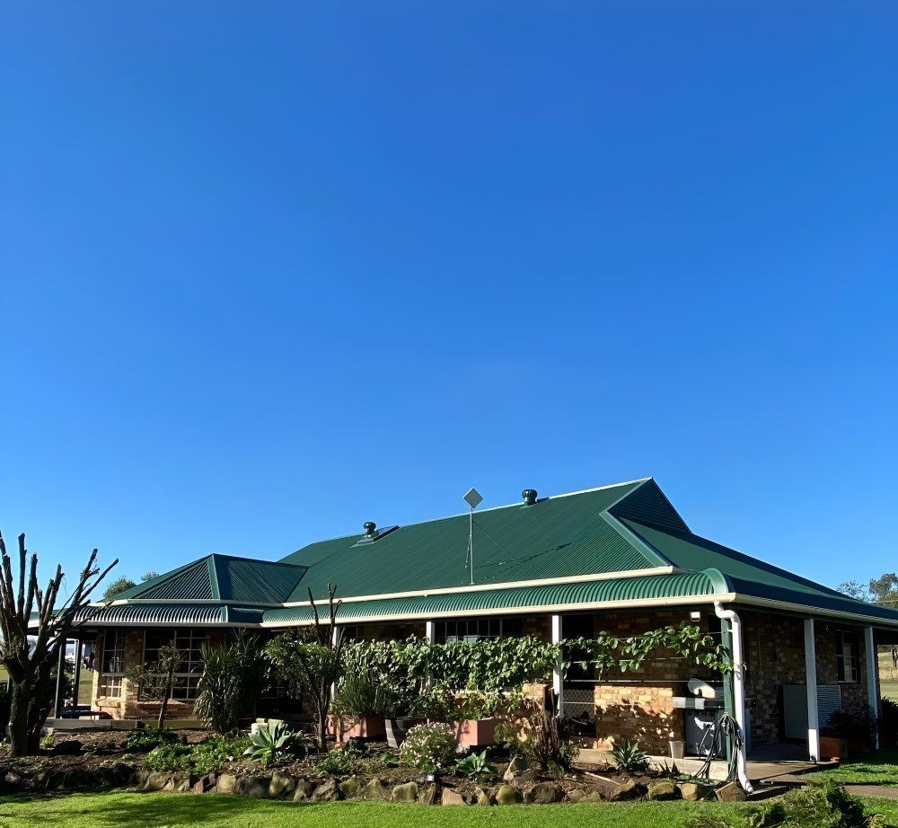 A House With a Green Roof and a Blue Sky in the Background — Lake Valley Roofing in Thornton, NSW