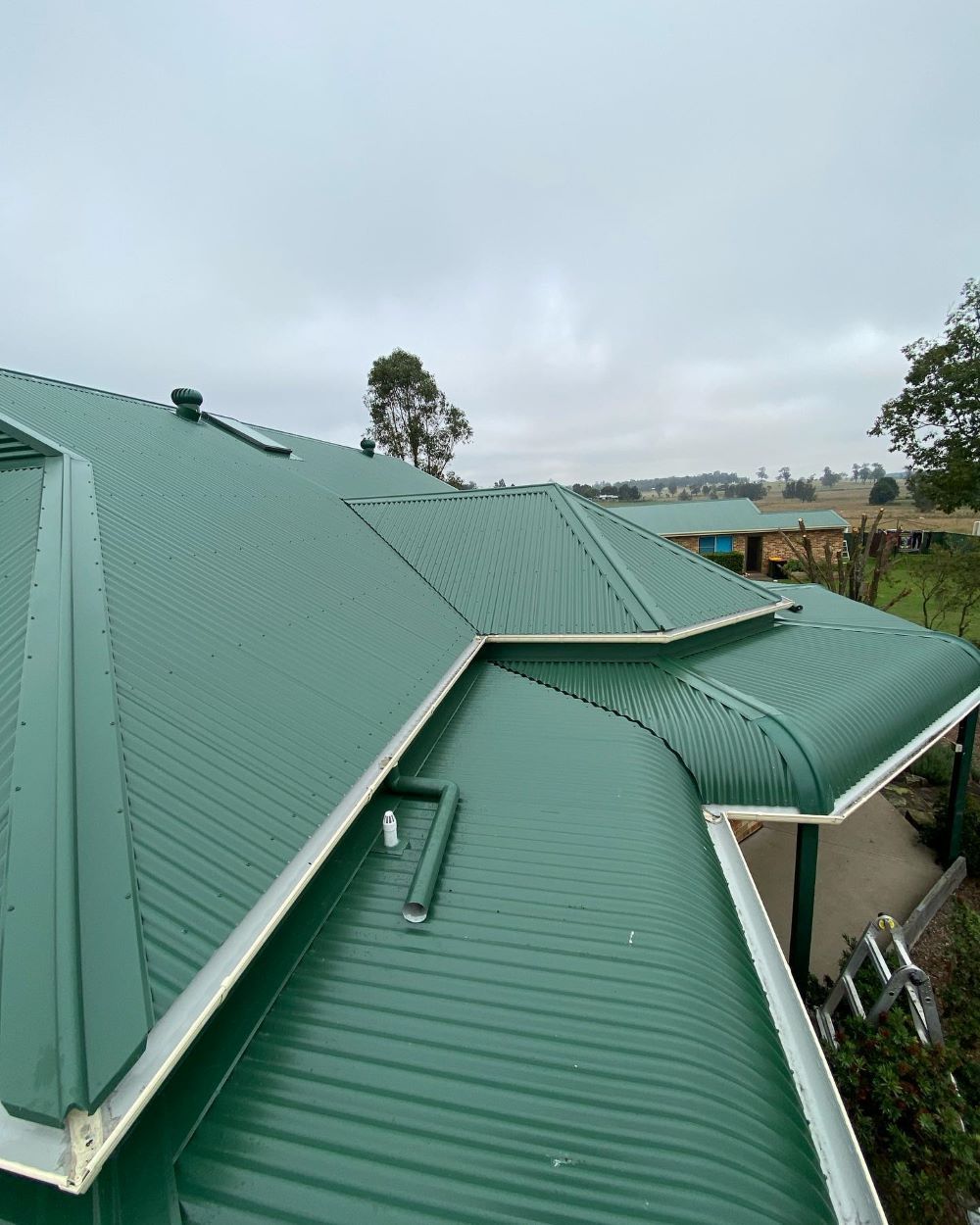 A Green Roof of a House With a White Trim on a Cloudy Day — Lake Valley Roofing in Bennetts Green, NSW