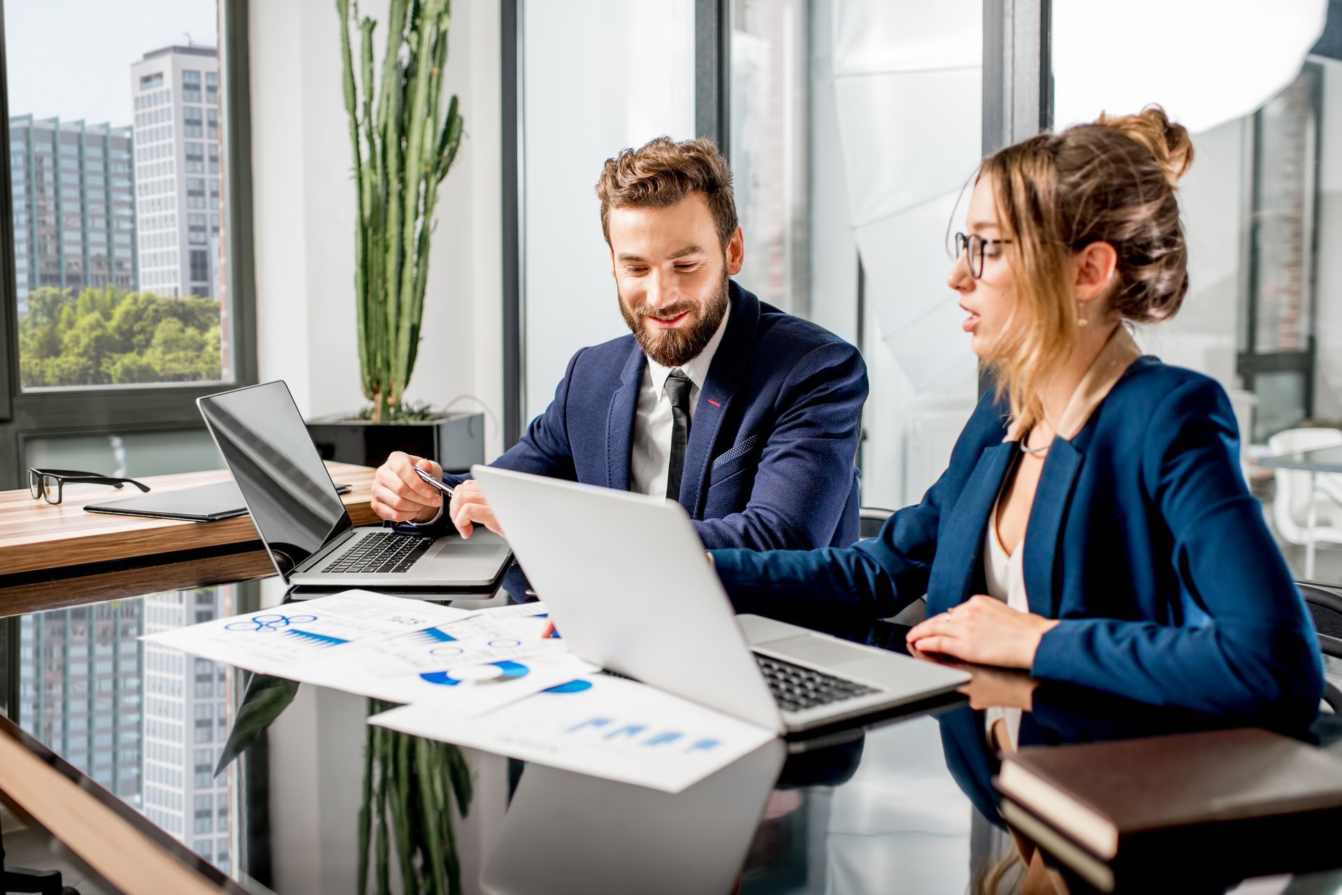 A man and a woman are sitting at a table with laptops.