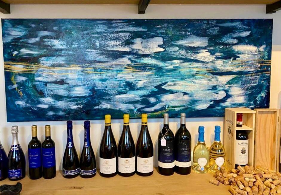 Bottles of wine lined up on a table with a large blue abstract painting in the background.