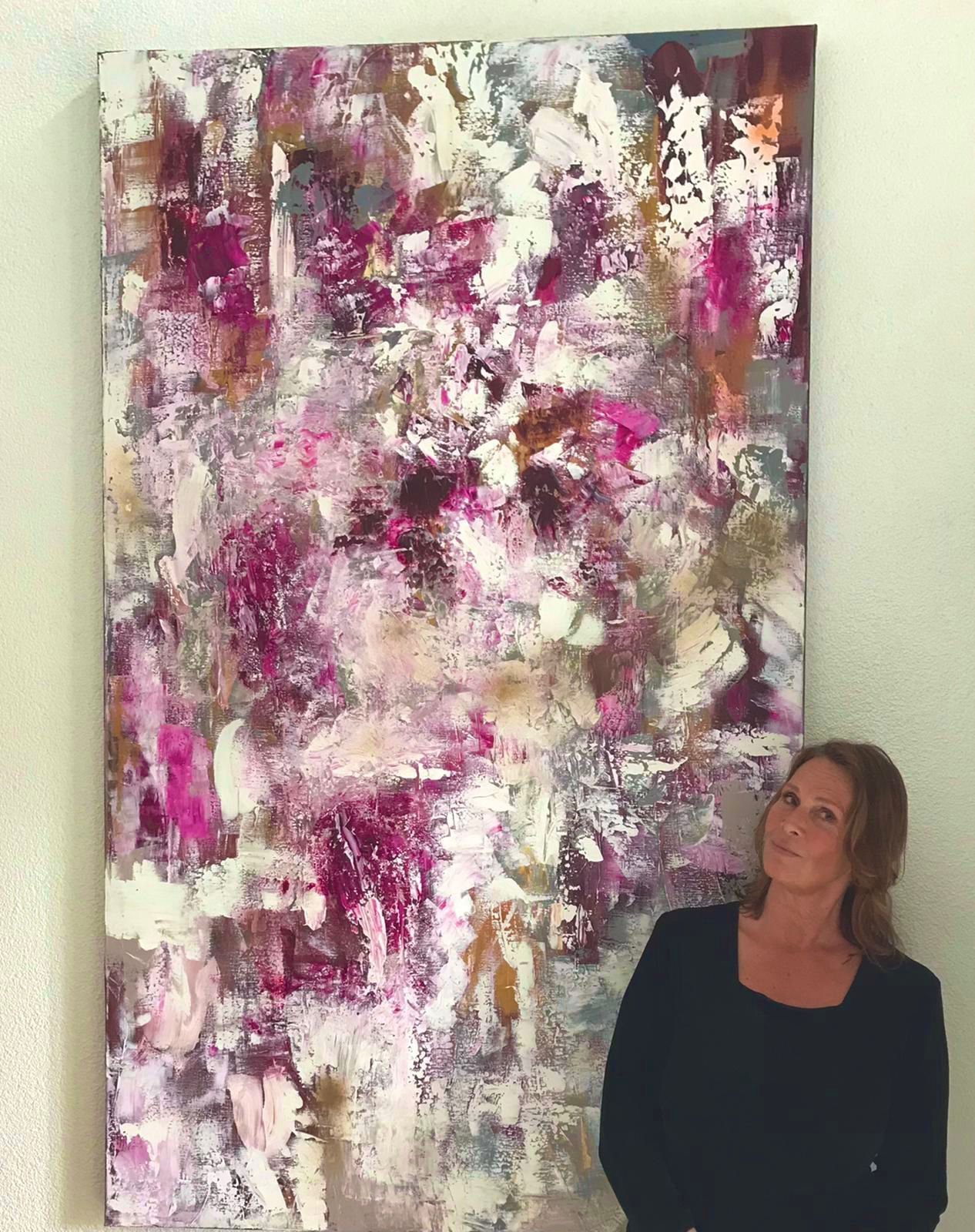 Woman standing next to abstract painting with shades of pink, white, and gold.