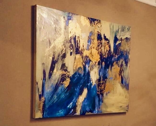 Abstract painting with blue, gold, and white brushstrokes on canvas, mounted on a brown wall.