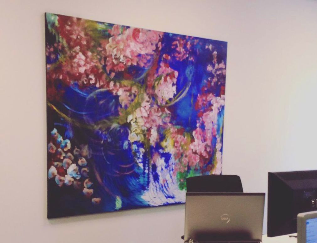 Abstract painting with pink and blue colors hanging on a white wall in an office setting.