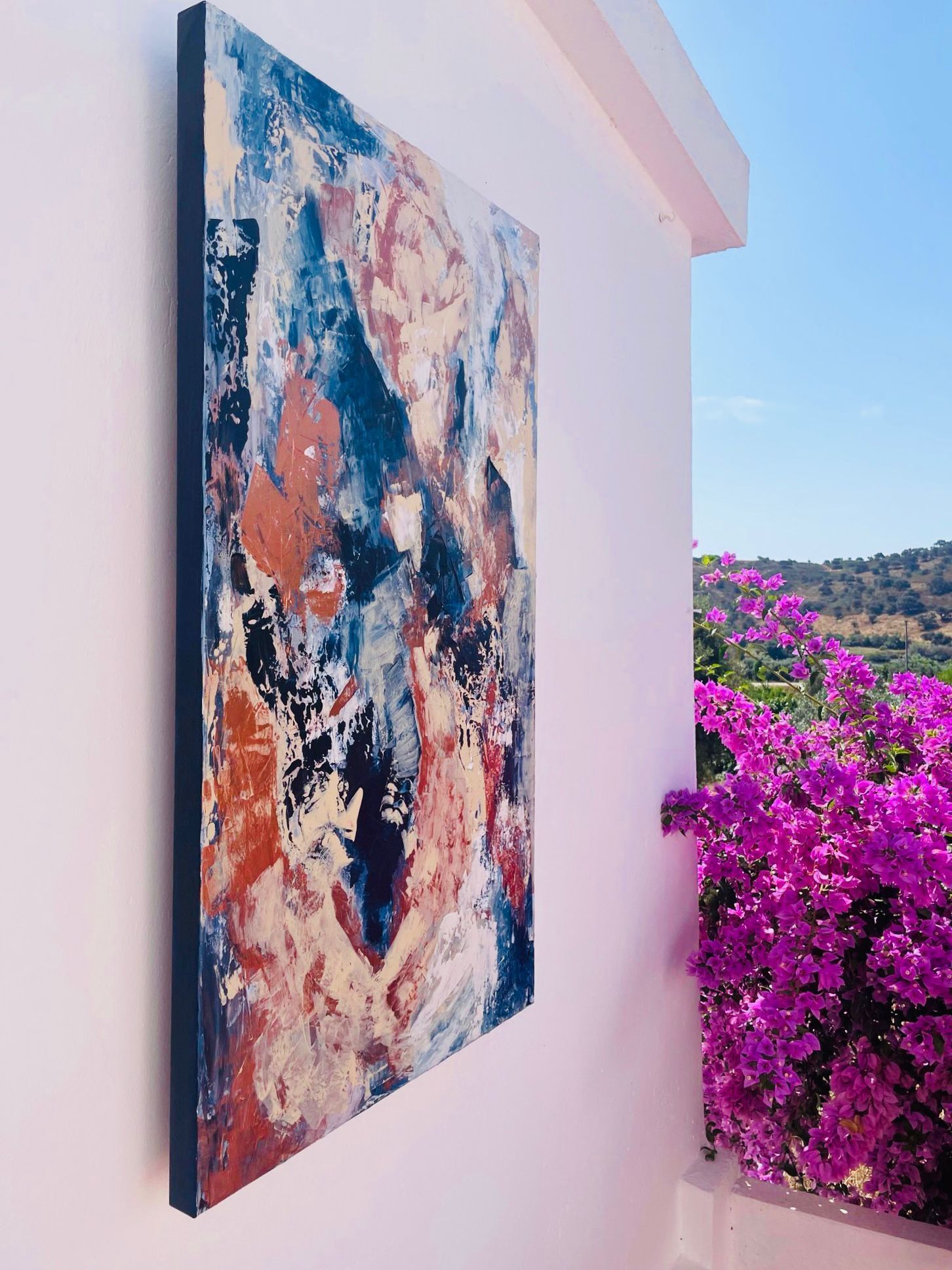 Abstract painting on a wall, with shades of blue, red, and white. Purple flowers and blue sky in the background.