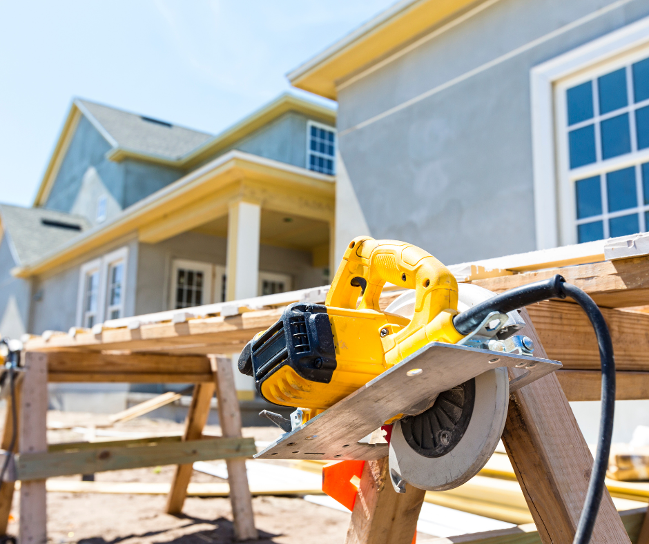 Yellow circular saw on a sawhorse at a house under construction, with a partially finished exterior.
