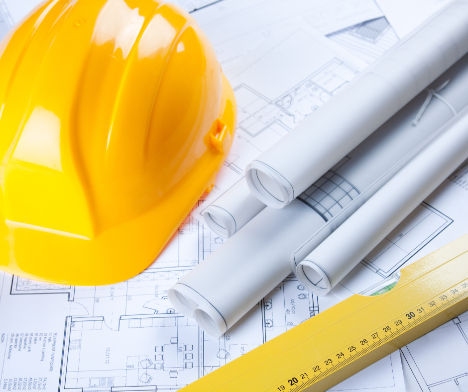 Yellow hard hat with rolled blueprints and a yellow measuring tape on architectural plans