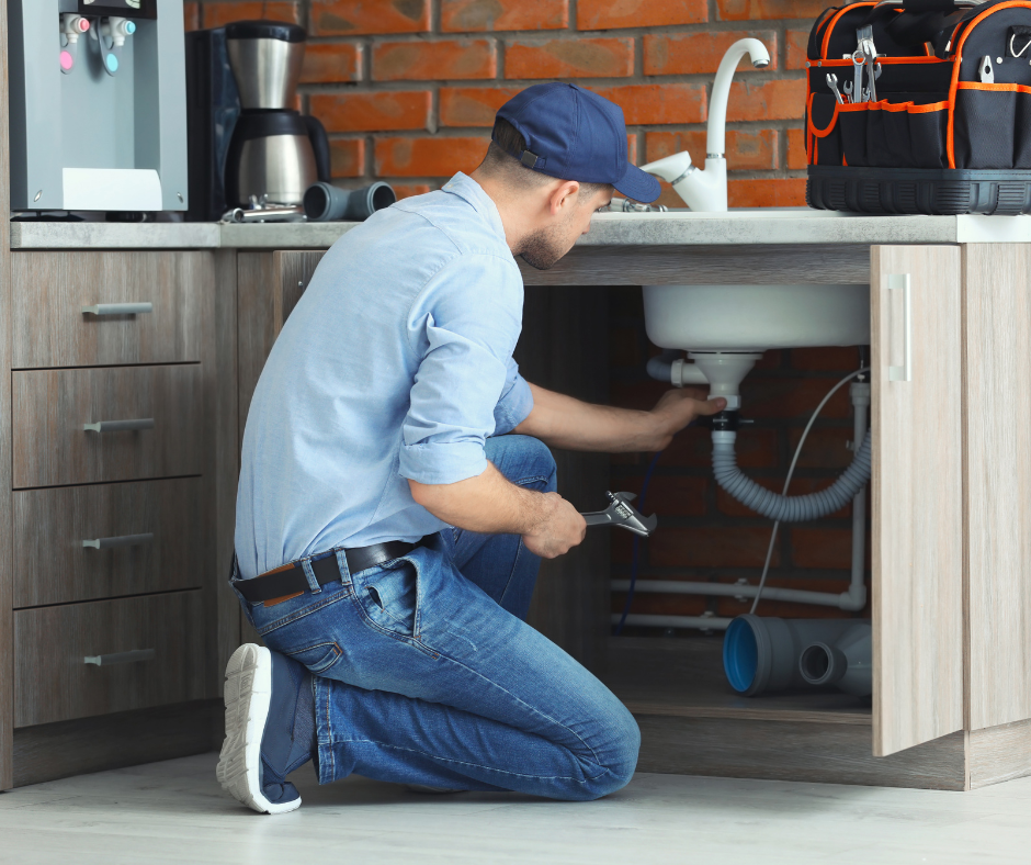 Plumber kneeling under kitchen sink, tightening pipes with a wrench in a modern kitchen