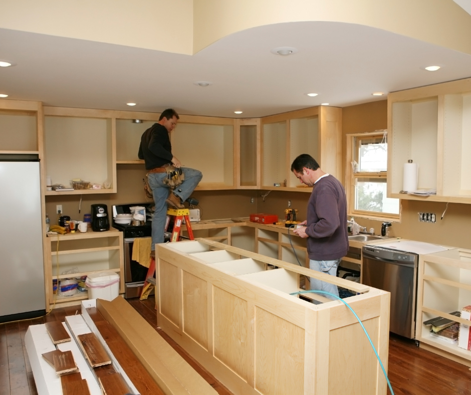 Two people installing a kitchen island in a bright, unfinished kitchen