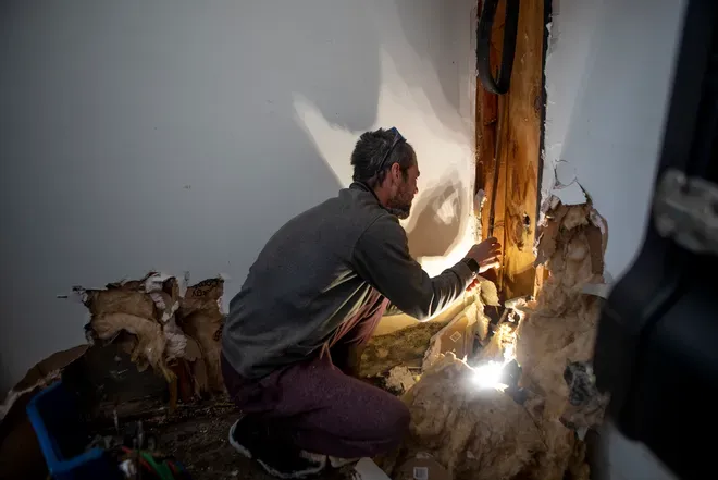A man is kneeling down in a room with a flashlight.