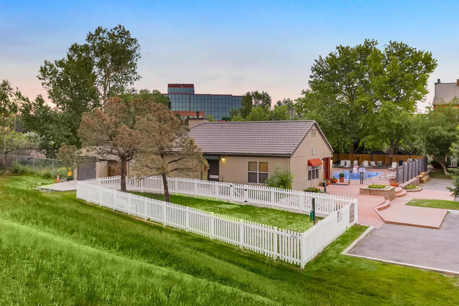 Fenced community pool area with a beige clubhouse and landscaped surroundings.