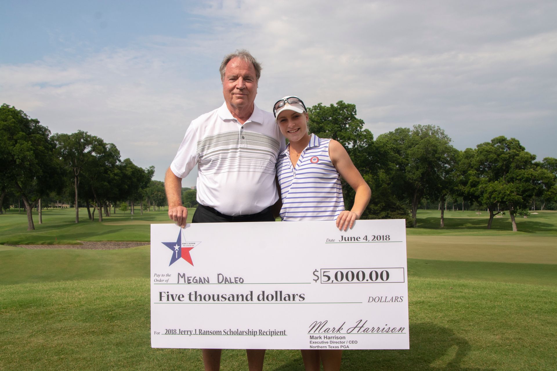 Two people holding a large $50,000 golf tournament check on a golf course