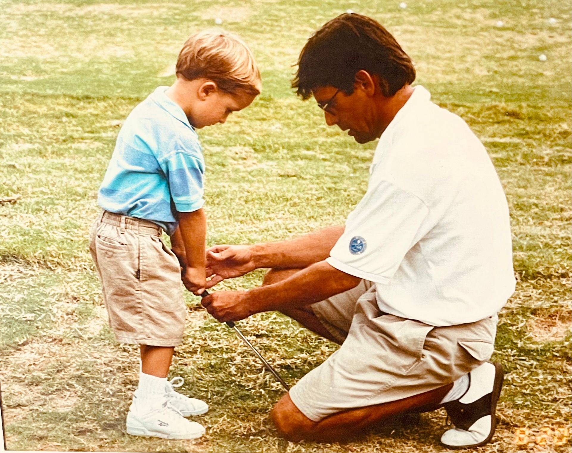 Man kneeling to tie a young child’s shoelaces on a grassy field