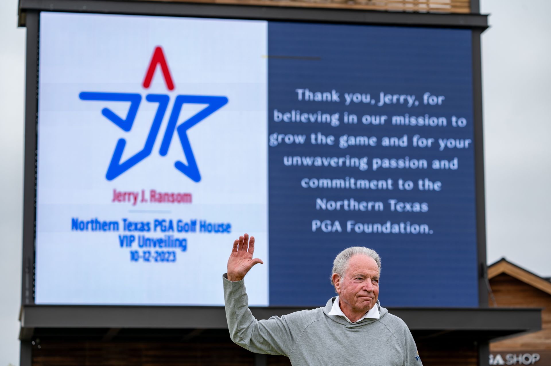Jerry J. Larson waves before a giant scoreboard with a thank-you message at Northern Texas PGA Golf House opening.