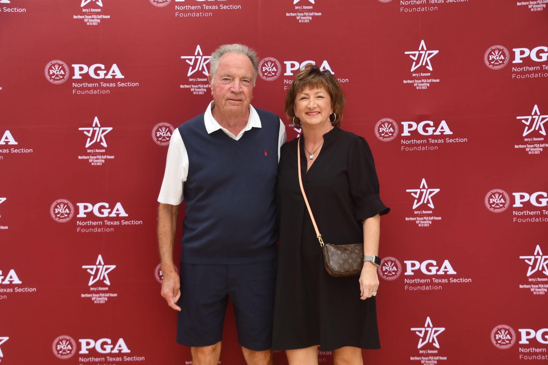 Two people posing in front of a red PGA backdrop at a golf event