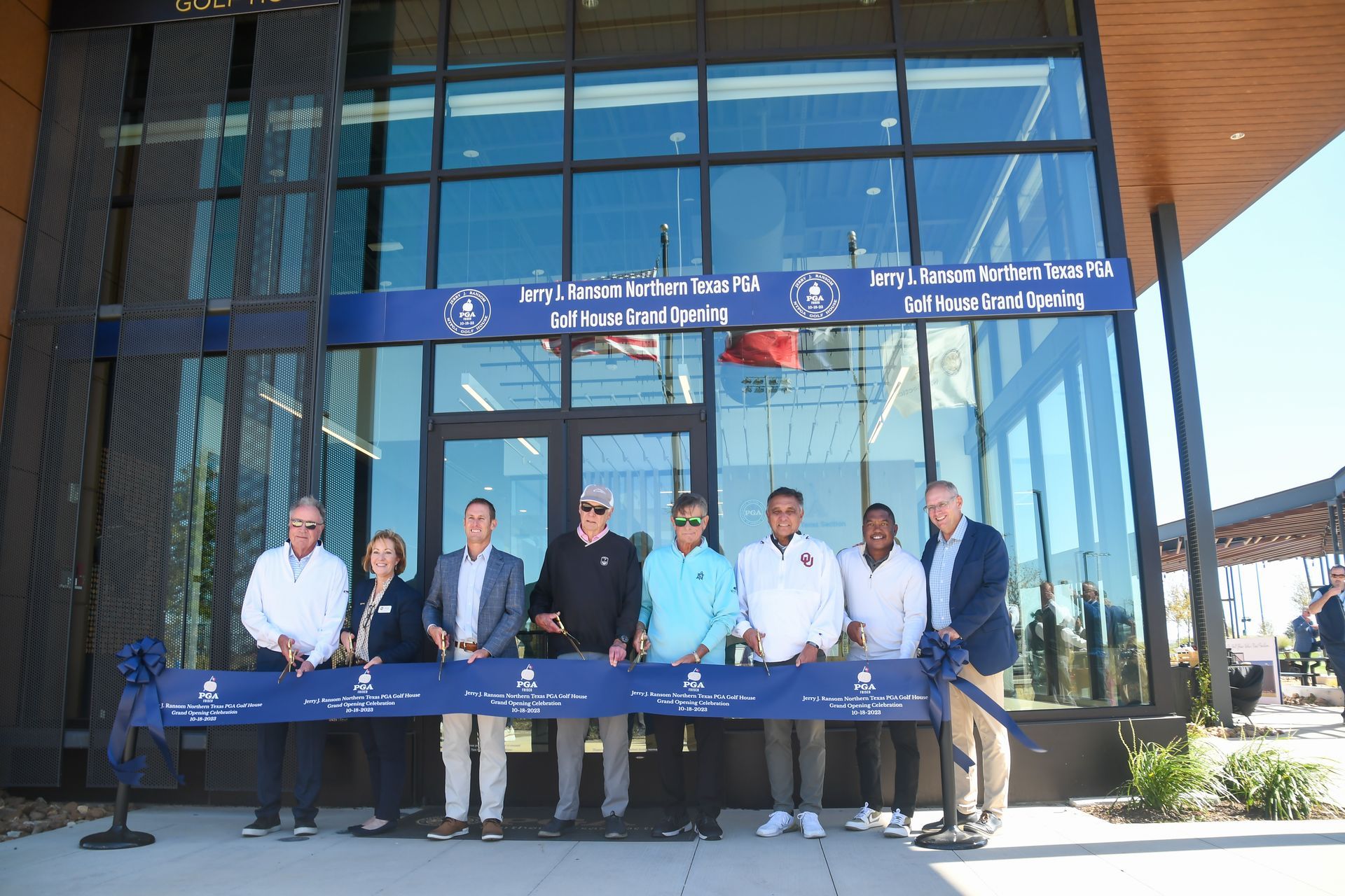 Group of people posing outside a glass building, holding a long blue banner at an event entrance