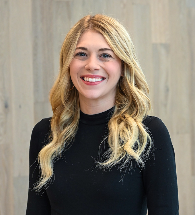 Smiling blonde woman in a black top against a light wood background