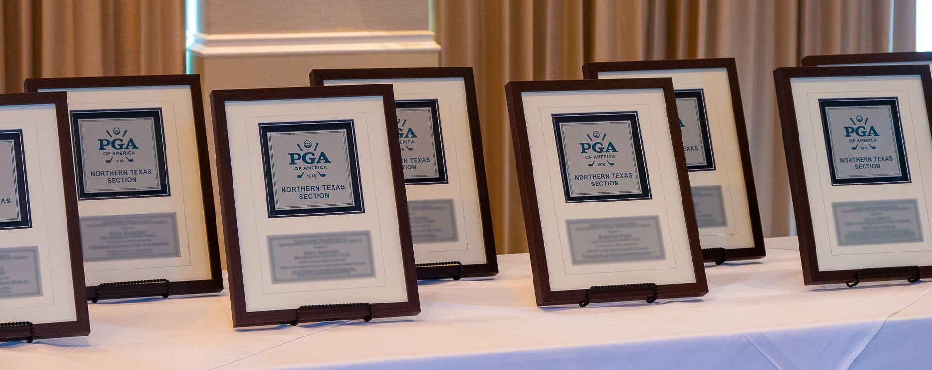 Framed certificates or awards lined up on a table at an indoor event