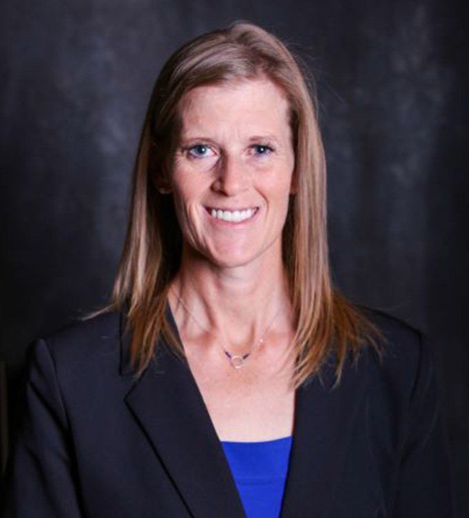 Studio portrait of a woman in a dark blazer and blue top, smiling against a dark backdrop
