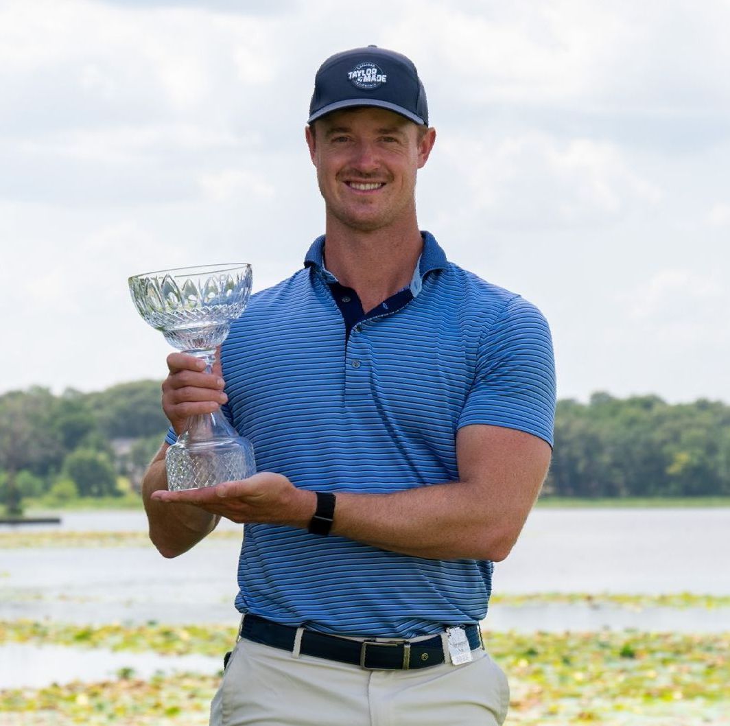 Golfer in blue shirt holding a trophy by a lake