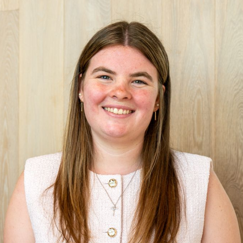 Smiling person in a white top standing against a light wood wall