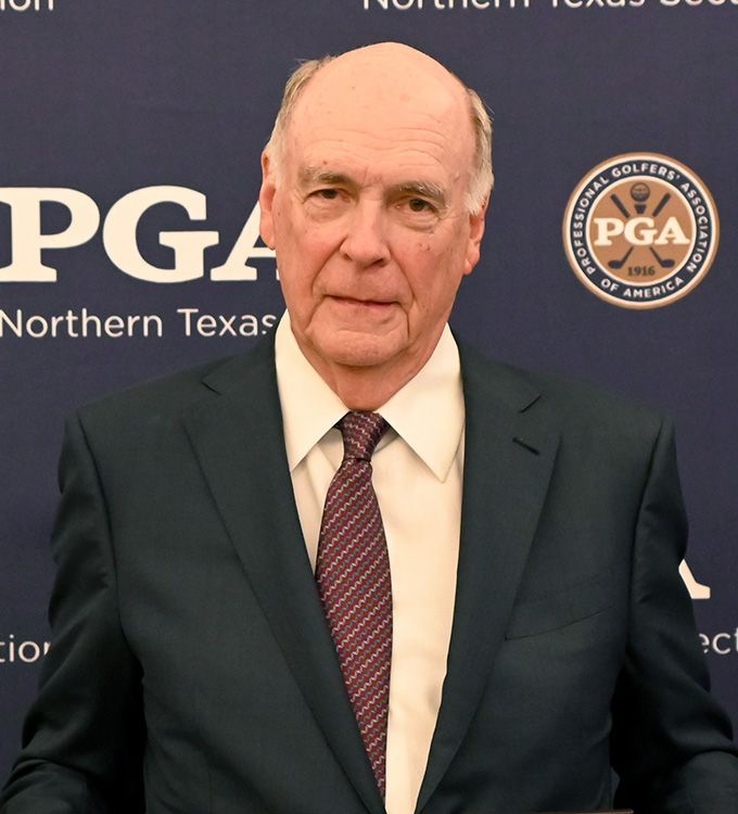 Man in a dark suit and maroon tie posing at a PGA Northern Texas event backdrop