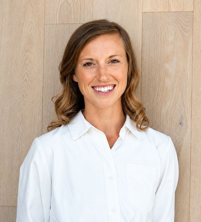 Smiling woman in a white blouse standing against a wood-paneled wall