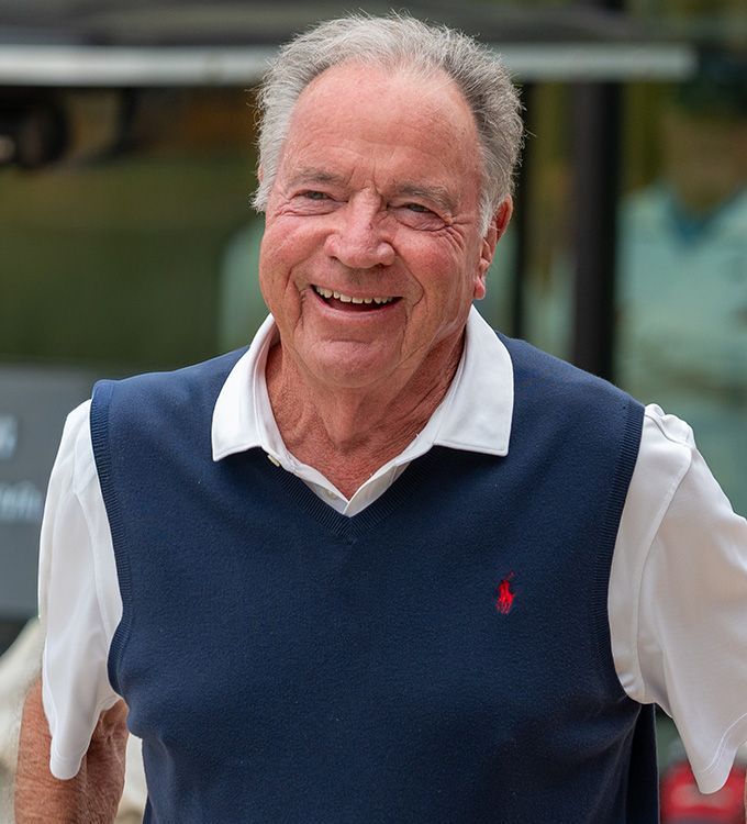Smiling man in a navy sweater vest over a white shirt, standing outdoors.