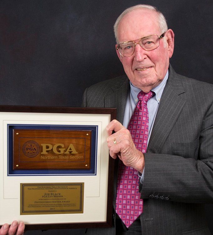 Man in suit holding a framed PGA plaque against a dark background