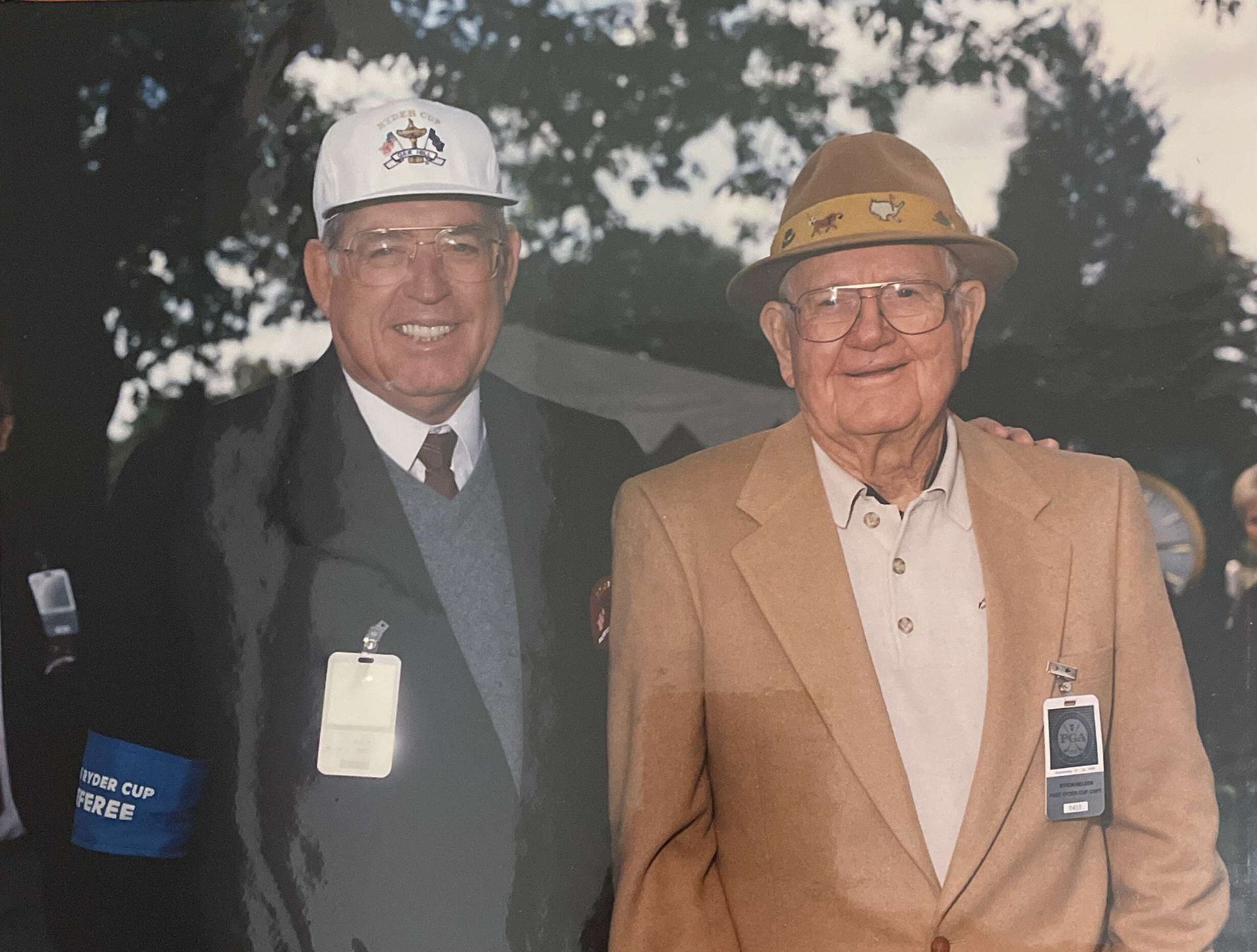 Two men in hard hats and jackets smiling outdoors, each wearing an ID badge.