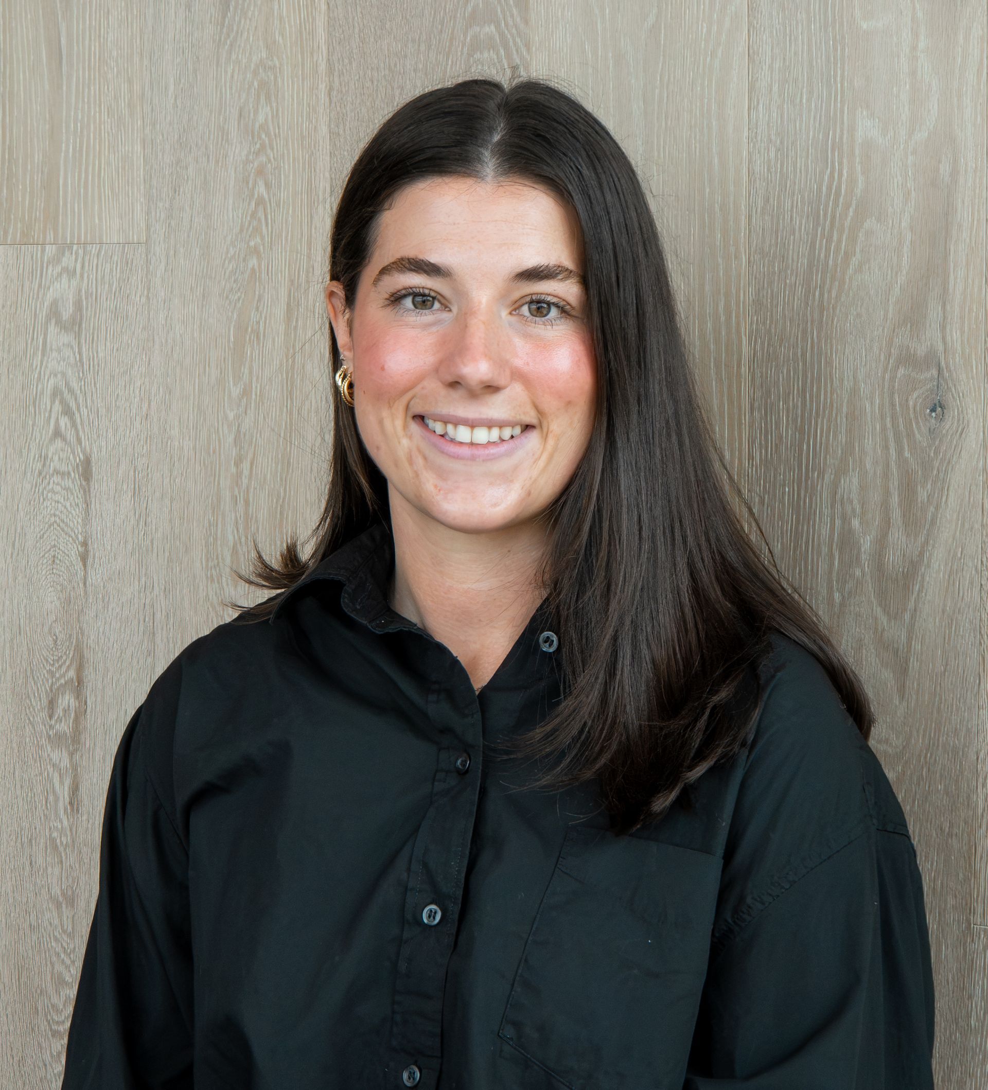 Smiling woman in a black shirt standing against a wood-paneled background