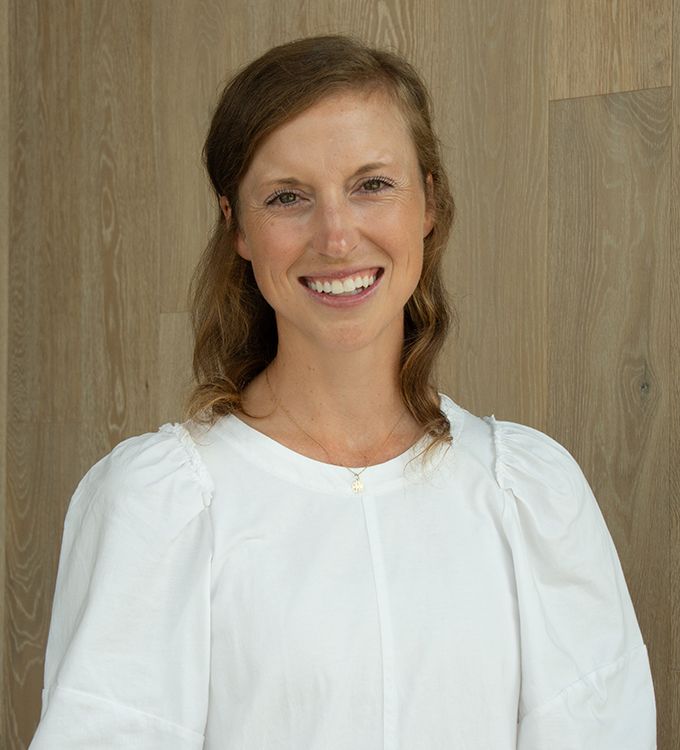 Smiling woman in a white blouse standing against a wood-paneled wall
