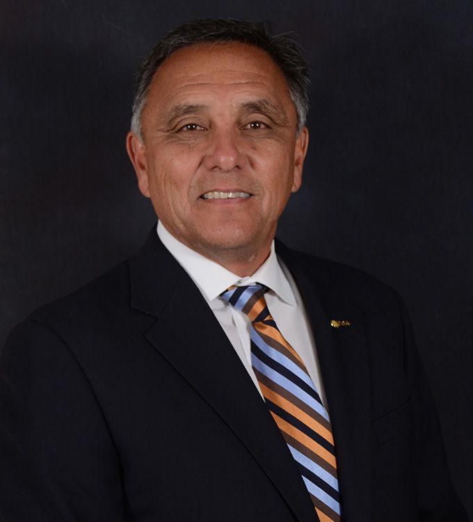 Portrait of a man in a dark suit with a striped tie against a dark background