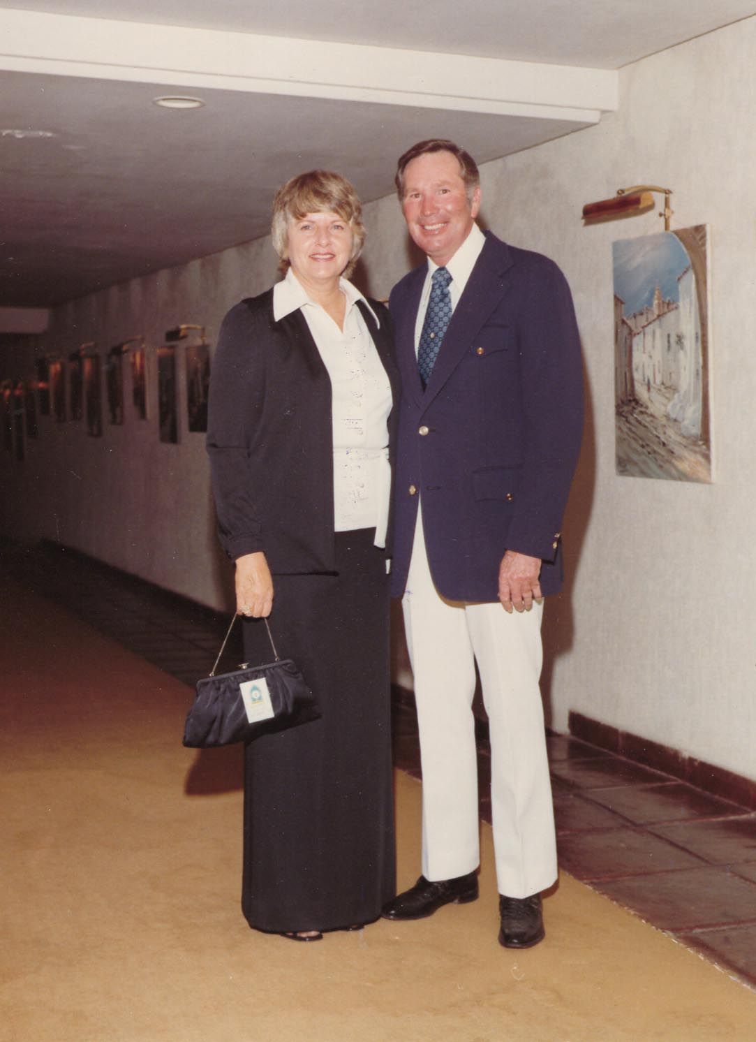 Two people posing in a hallway, dressed formally and standing side by side.