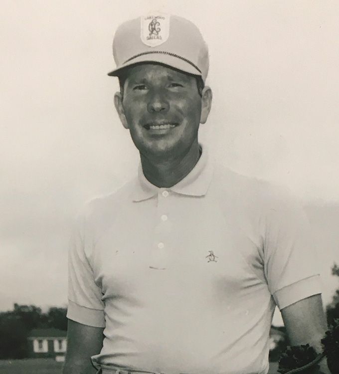 Man in a white polo and cap smiling outdoors on a golf course