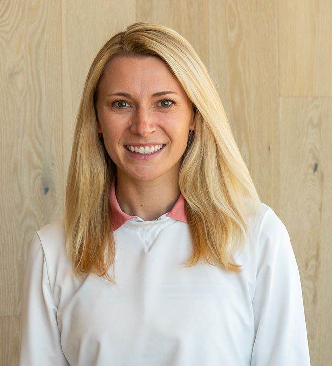 Smiling blonde woman in a white shirt standing against a light wood wall