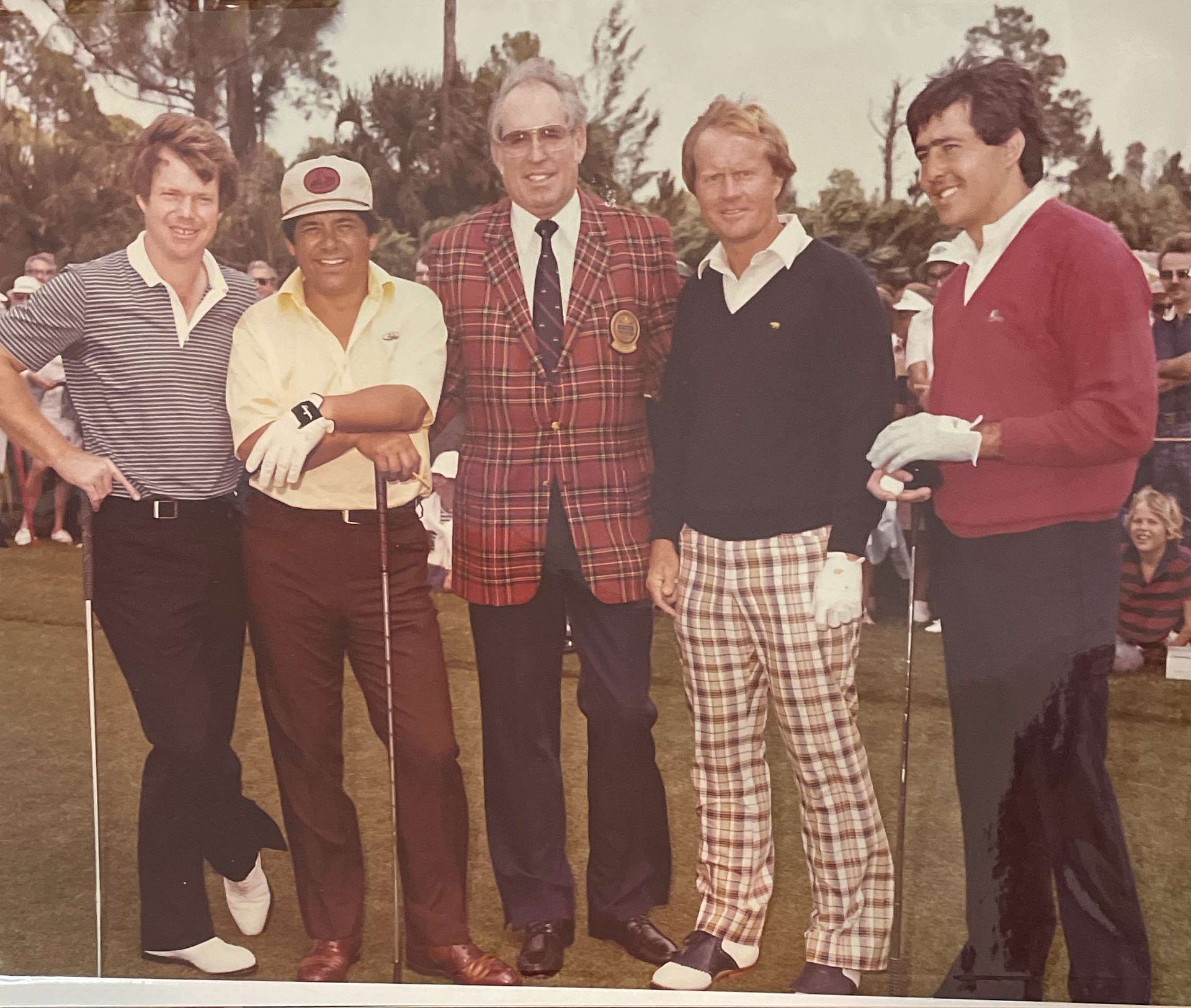 Five men standing outdoors with golf clubs, wearing colorful sweaters and plaid pants on a course