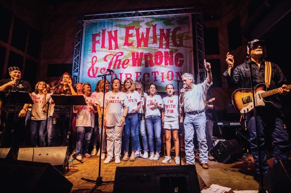 Group of people on a stage under red lights, singing and posing in front of a banner.