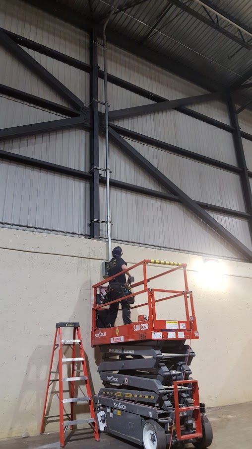 A man is standing on a scissor lift in a warehouse.