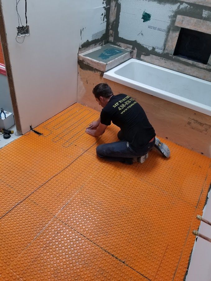 A man is kneeling on the floor in a bathroom next to a bathtub.