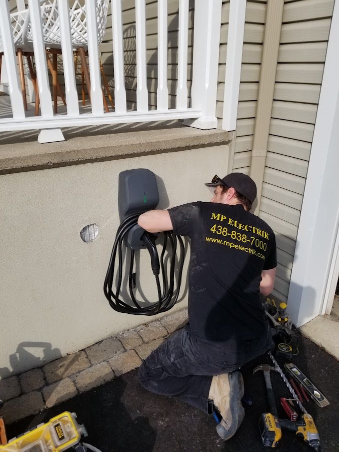 A man is kneeling down in front of a house holding a cord.