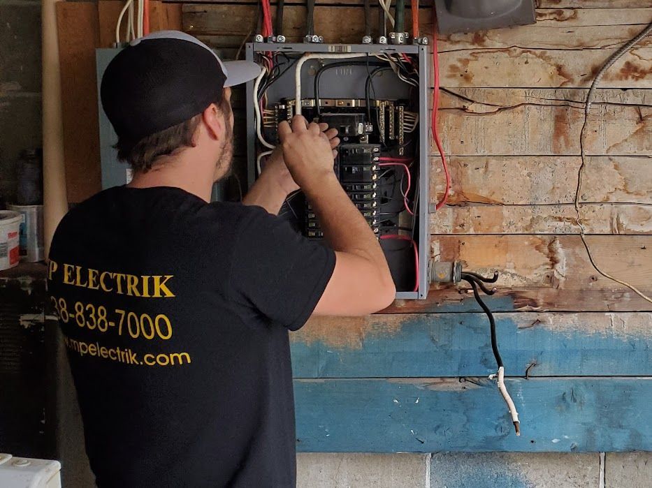 A man wearing a black shirt that says electrick is working on an electrical box