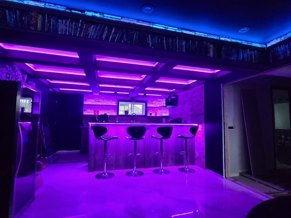 A bar with purple lights on the ceiling and stools.
