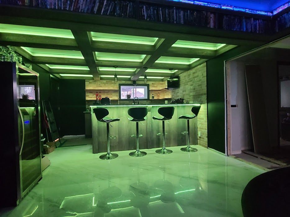 A kitchen with a bar and stools and green lights on the ceiling.