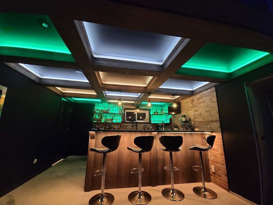A bar with stools and green lights on the ceiling