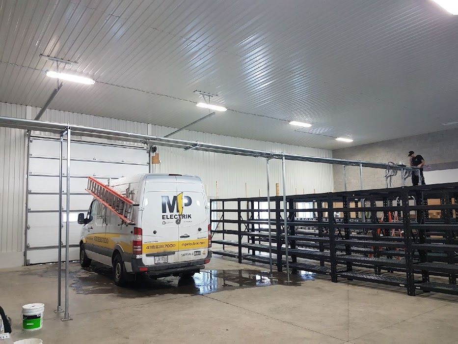 A white van with a ladder on the back is parked in a garage.