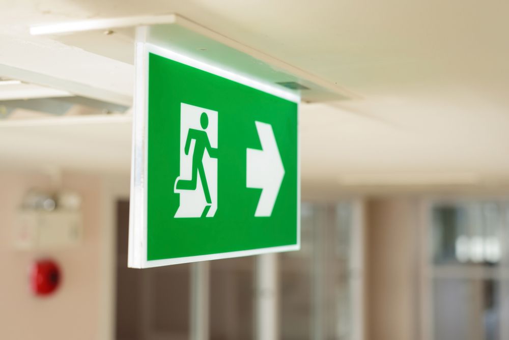 A Green Exit Sign Is Hanging from The Ceiling in A Hallway — Test Right Services in Kirwan, QLD