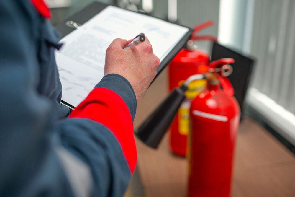 A Man Is Writing on A Clipboard Next to Fire Extinguishers — Test Right Services in Townsville, QLD