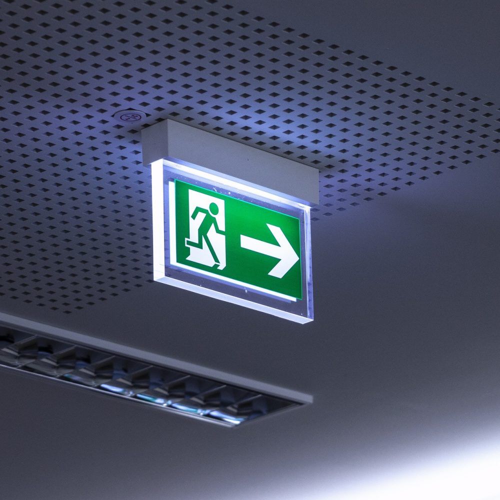 Green and white emergency exit sign, illuminated, mounted on a ceiling.— Test Right Services in Ingham, QLD