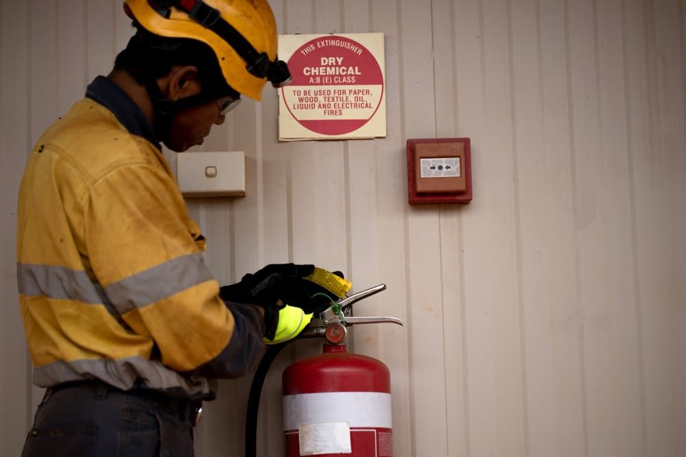 A Man Wearing a Hard Hat Is Using a Fire Extinguisher — Test Right Services in Kirwan, QLD